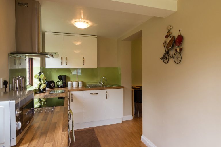 Modern kitchen with white cupboards, inbuilt cooker and hob, small kitchen appliances, window, Tilshead grounds, with garden furniture and wooden cabin, Brades Acre Camping Site, Stonehenge, Wiltshire, Salisbury, camping, holiday lodges